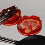 Red flower-shaped spoon rests with tongs on a white surface