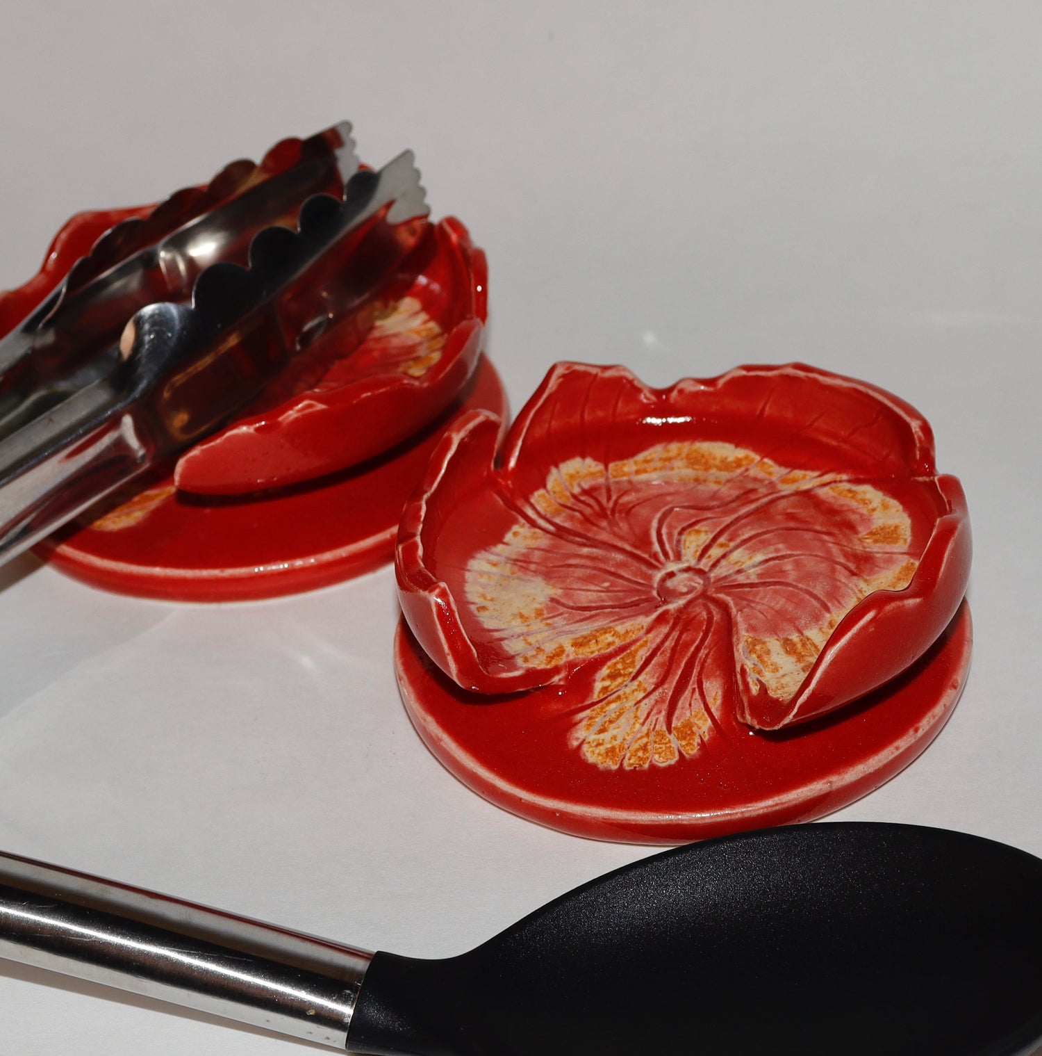 Red flower-shaped spoon rests with tongs on a white surface